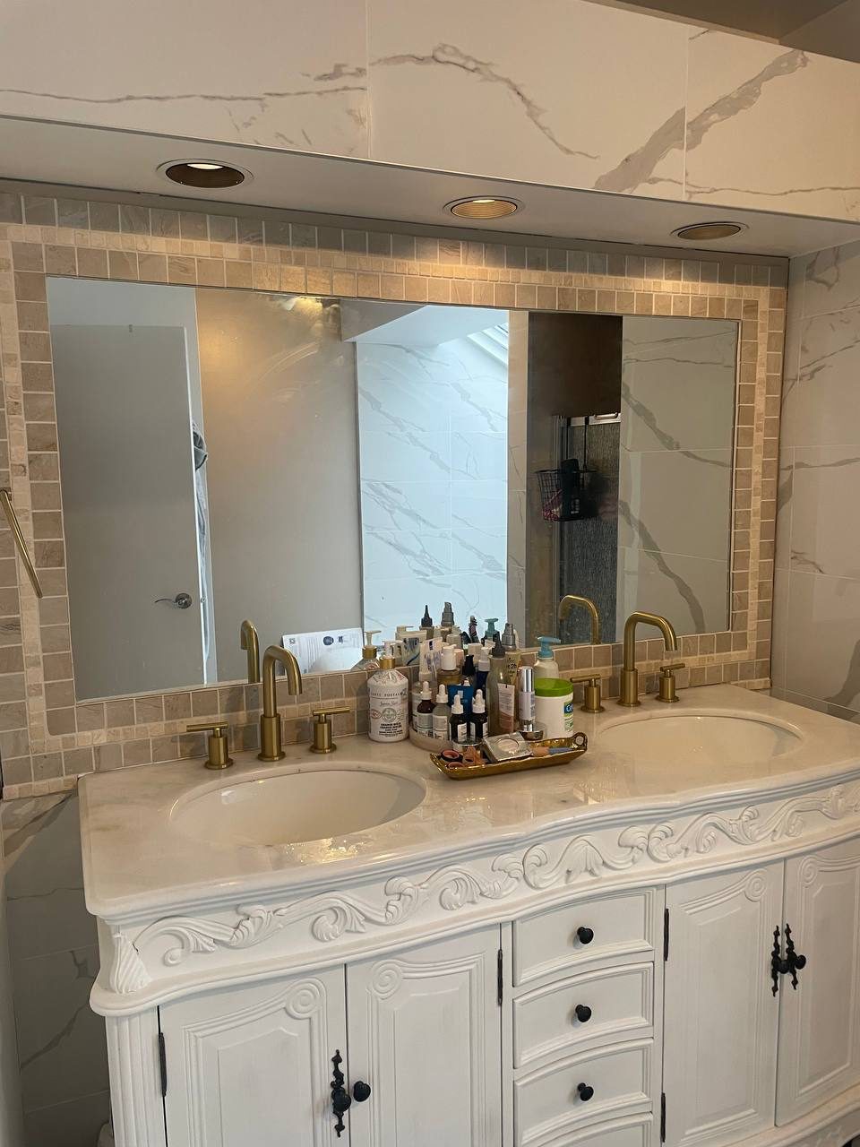 Renovated bathroom with double vanity, marble tiles and gold faucets by Reno Island